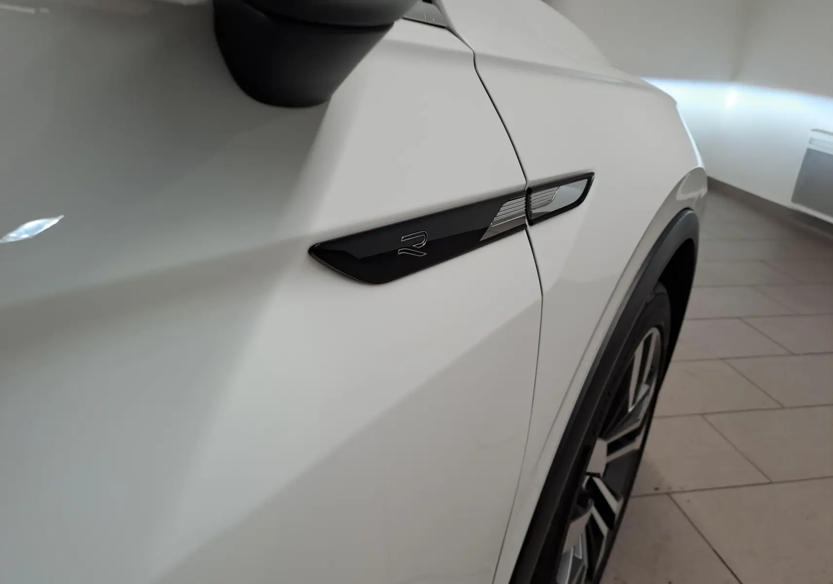 Gros plan sur l'aile avant droite blanche du Volkswagen Tiguan 2.0 TDI R-Line avec logo "R" noir et jante alliage visible.