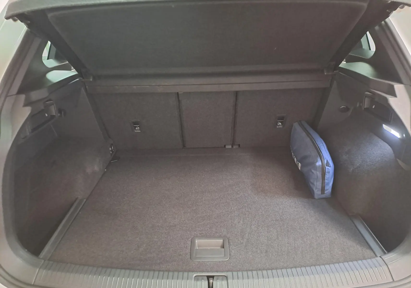 Coffre ouvert du Volkswagen Tiguan blanc pur 2023, vue arrière montrant un espace de chargement avec trousse bleue.