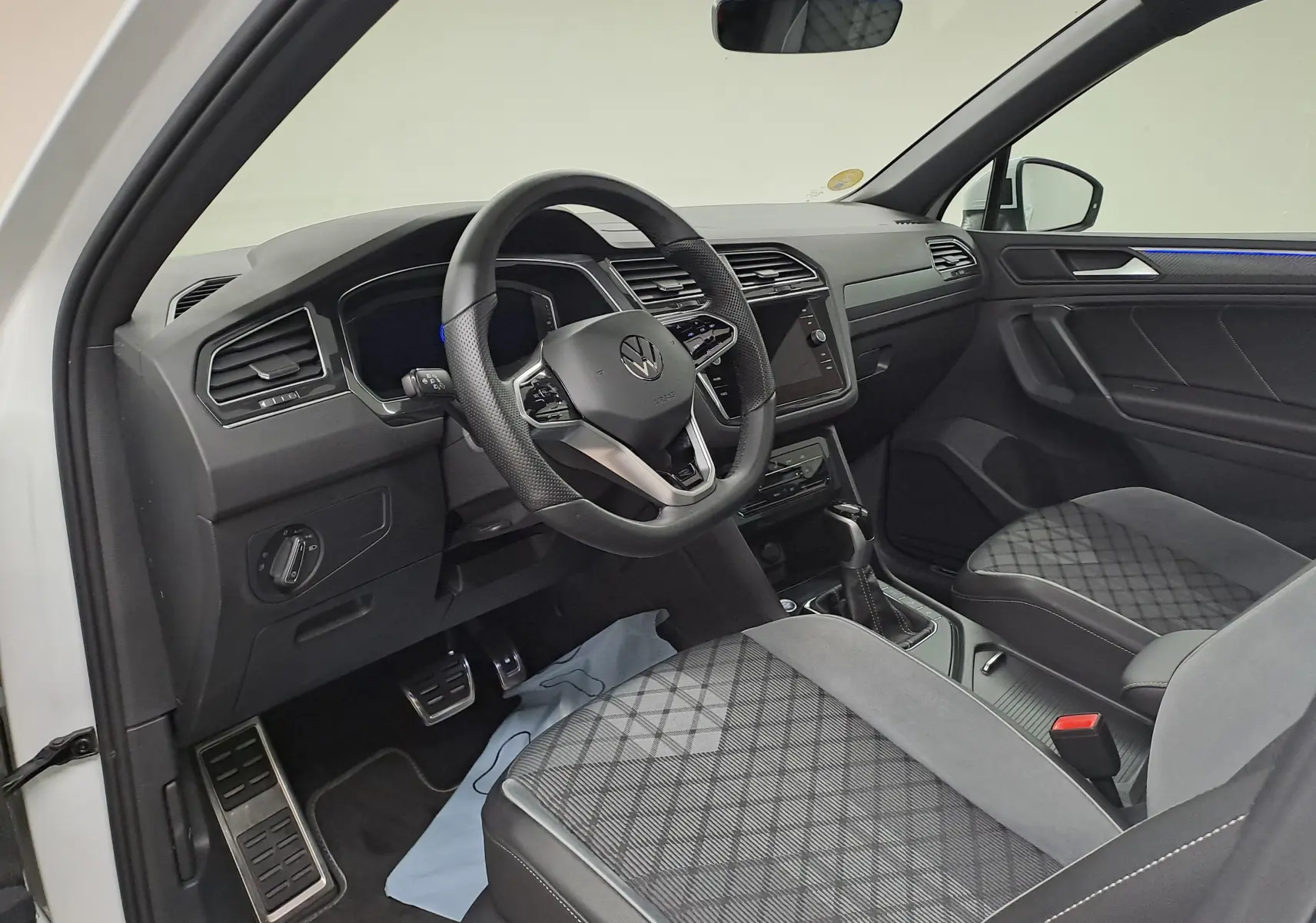 Vue intérieure côté conducteur du Volkswagen Tiguan 2023 avec volant sport, sièges tissu noir et éclairage d'ambiance bleu.