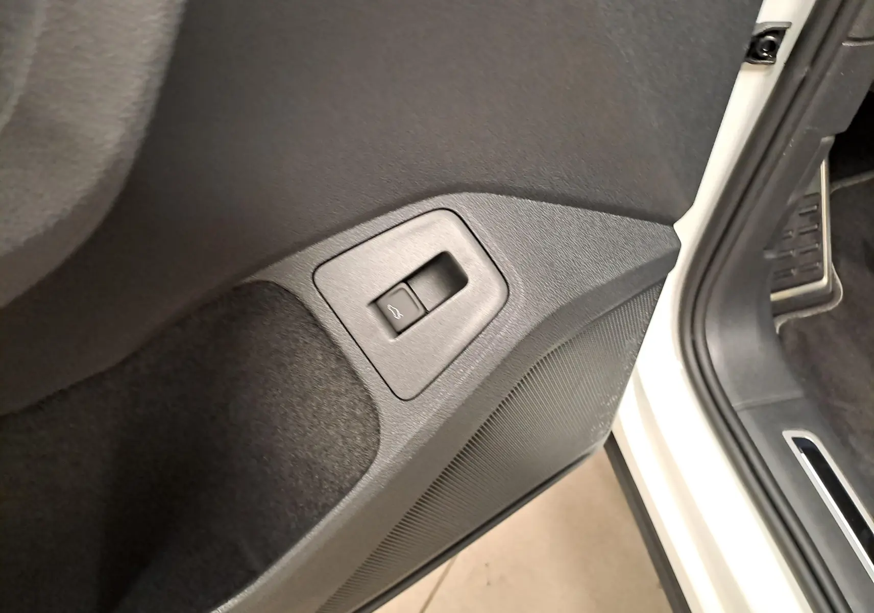 Détail du bouton d'ouverture du coffre sur la porte côté conducteur d'un Volkswagen Tiguan blanc pur 2023.