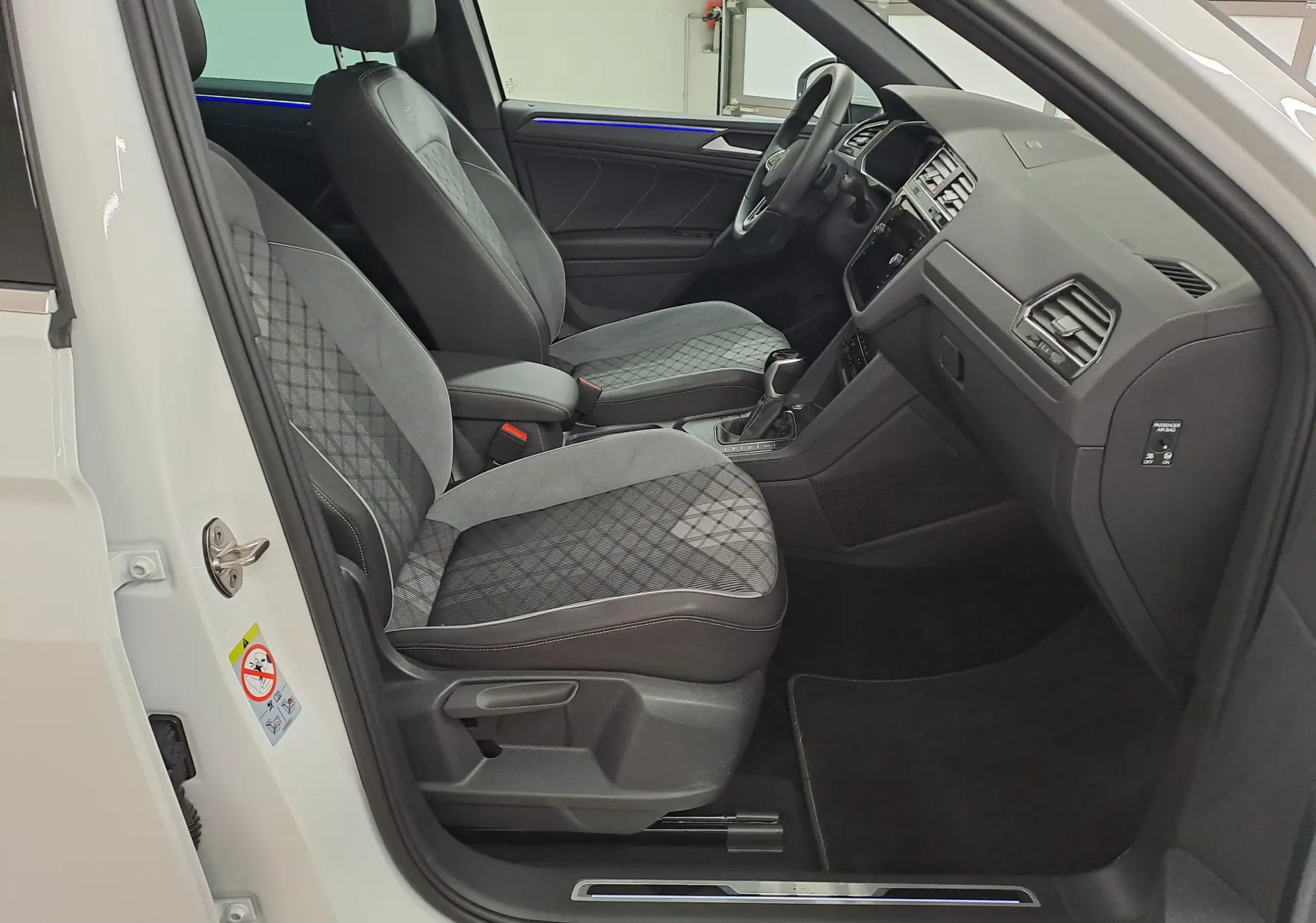 Vue intérieure côté conducteur du Volkswagen Tiguan blanc pur 2023, sièges sport gris à motifs et tableau de bord noir.