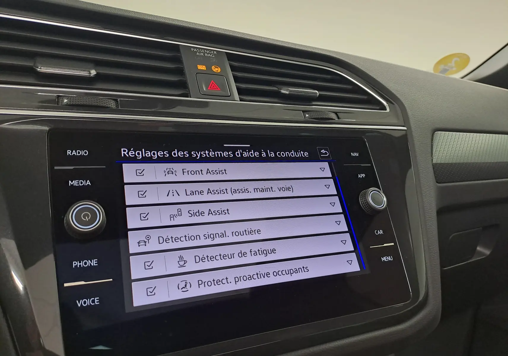 Vue rapprochée de l'écran tactile central du Volkswagen Tiguan 2023 affichant les réglages des aides à la conduite.