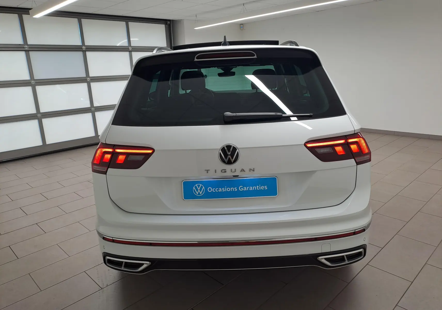 Vue arrière d'un Volkswagen Tiguan blanc pur 2023 avec feux LED allumés et double sortie d'échappement intégrée.
