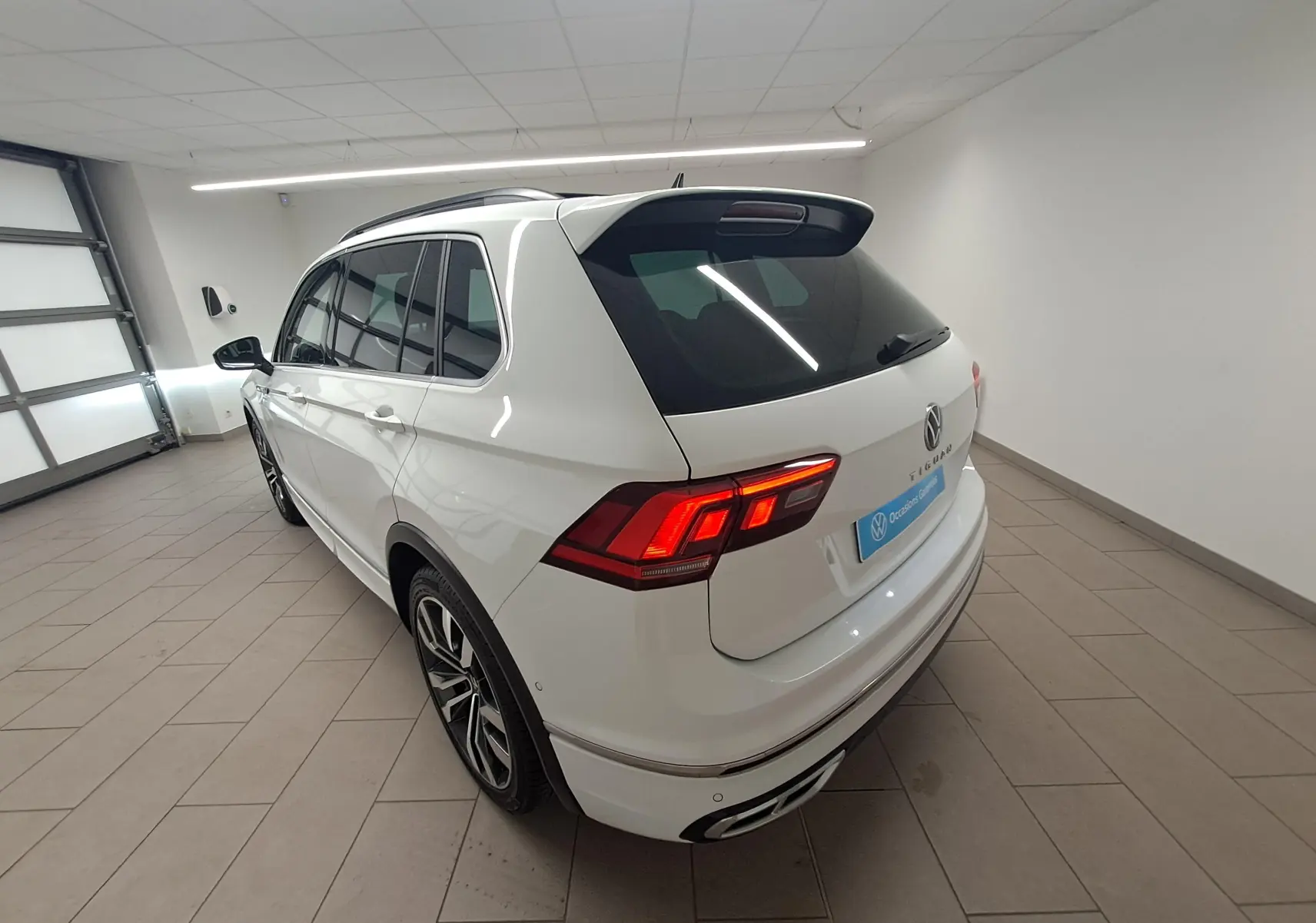 Volkswagen Tiguan blanc pur en 3/4 arrière droit, avec jantes alliage 20'' et toit ouvrant panoramique visible.