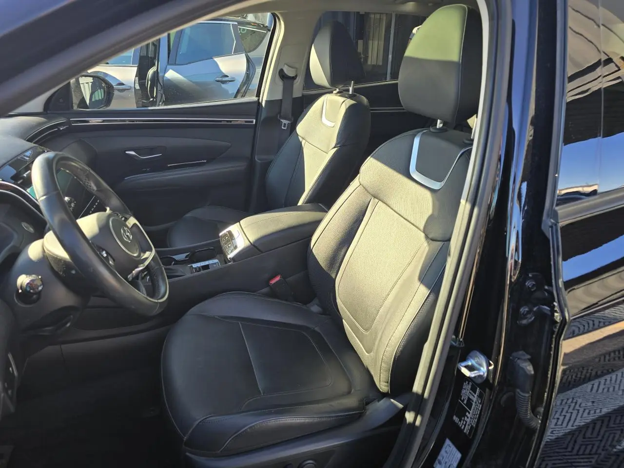 Vue intérieure côté conducteur du Hyundai Tucson noir Phantom Metal, mettant en valeur les sièges en cuir et la console centrale.