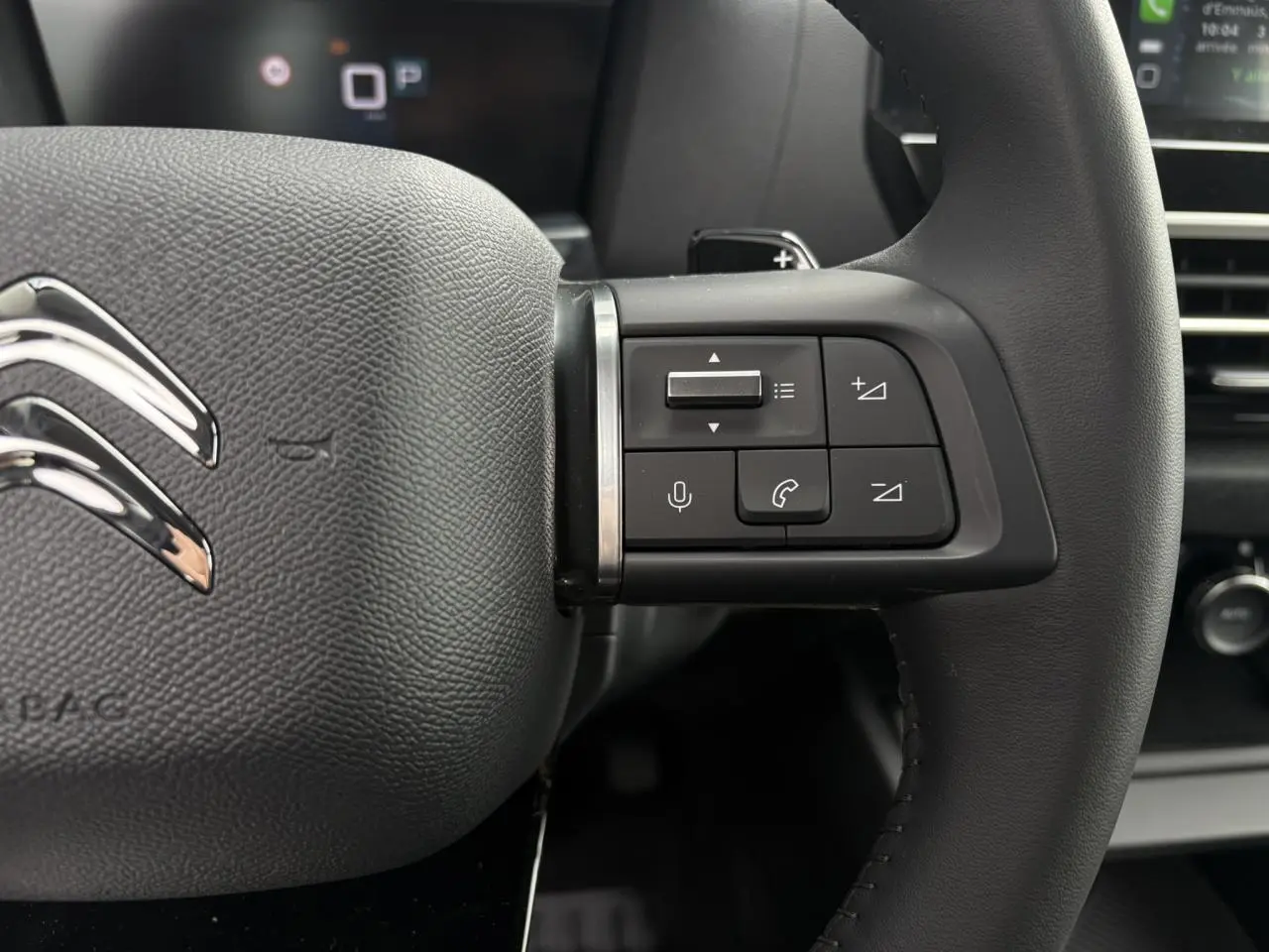 Gros plan sur le volant cuir noir de la Citroën C4 2024 avec commandes audio et logo chromé visible.
