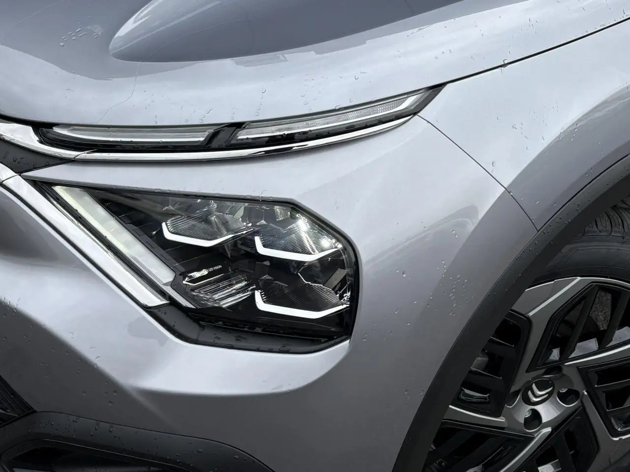 Gros plan sur le phare avant gauche LED et la jante alliage noire du Citroën C4 gris acier 2024.
