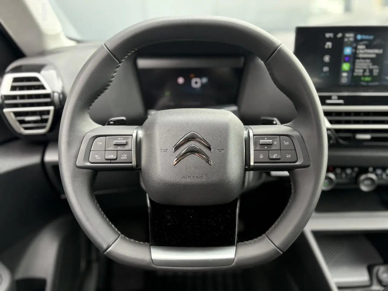 Vue rapprochée du volant en cuir noir de la Citroën C4 2024 avec commandes intégrées et tableau de bord numérique.