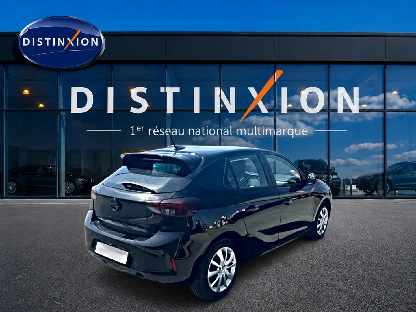 Opel Corsa noire vue en 3/4 arrière droit, avec becquet et jantes alliage devant une vitrine Distinxion.