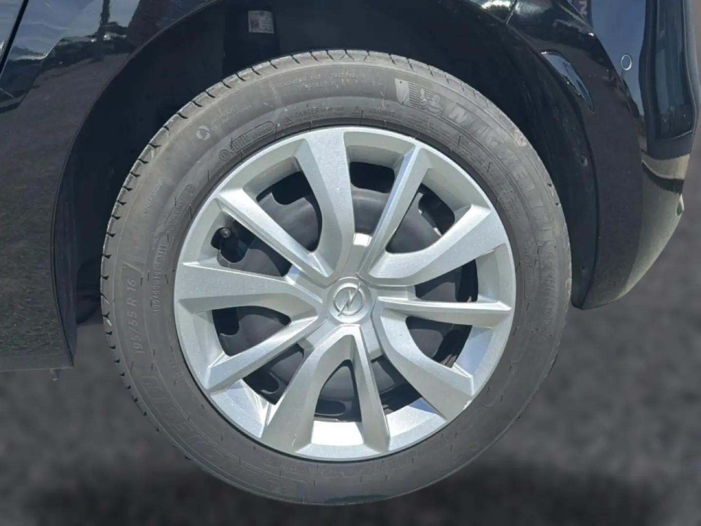 Gros plan sur la roue avant droite d’une Opel Corsa noire, avec enjoliveur argenté et logo Opel au centre.