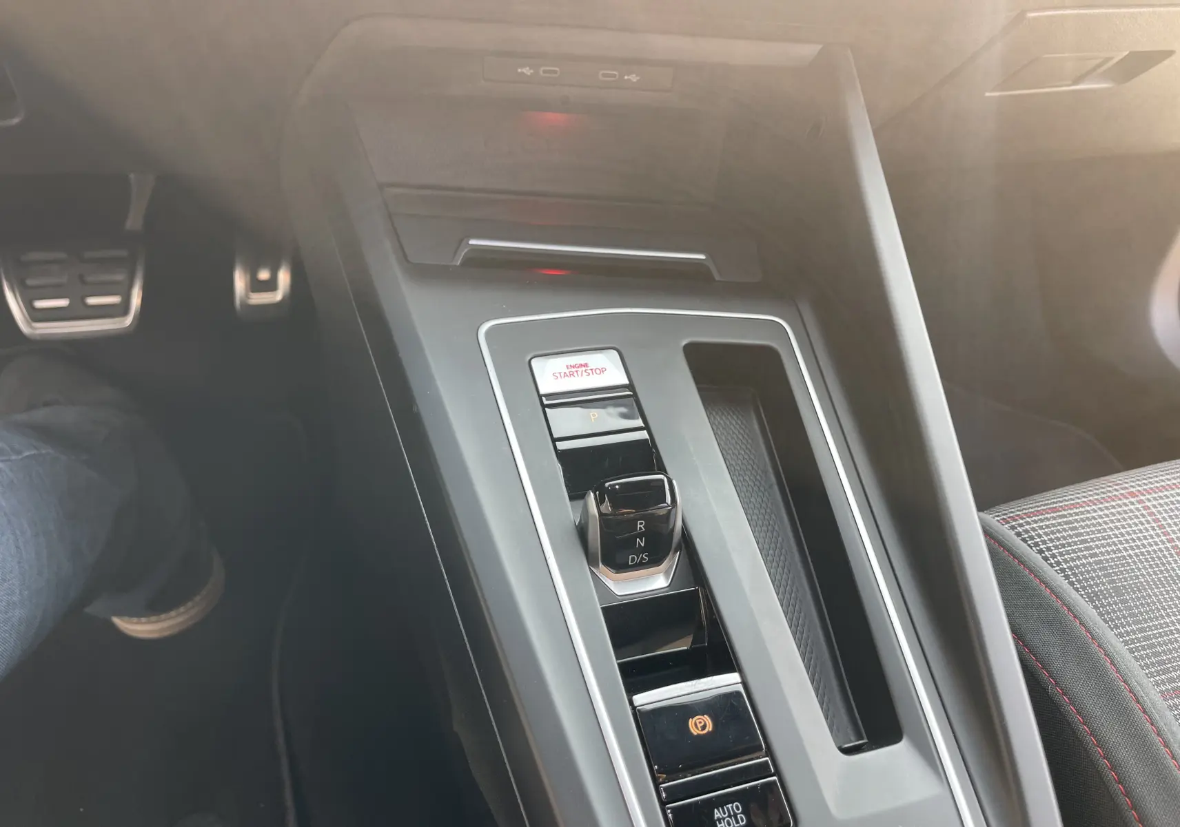 Vue rapprochée de la console centrale de la Volkswagen Golf VIII GTI 2021 avec levier de vitesse DSG et siège tissu à surpiqûres rouges.