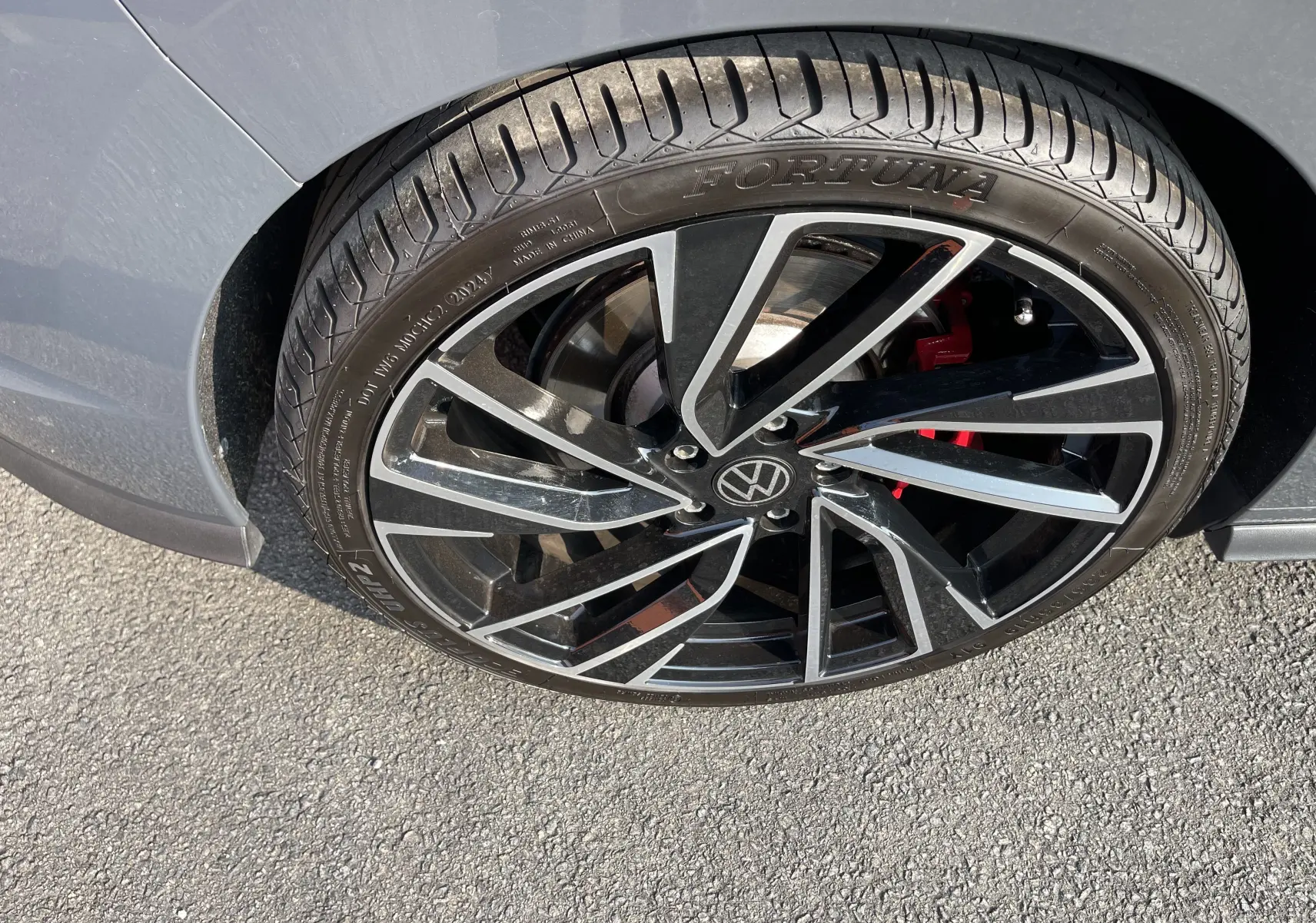 Gros plan sur la roue avant droite grise d'une Volkswagen Golf VIII GTI avec jante noire et détails rouges du frein.