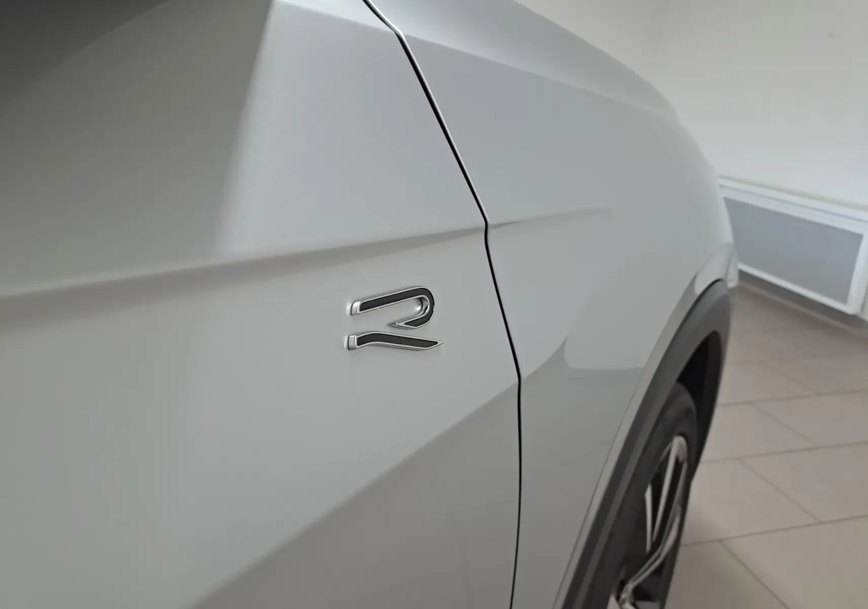 Gros plan sur l'aile avant droite argentée du Volkswagen T-Cross 2025 avec logo R et jante alliage visible.
