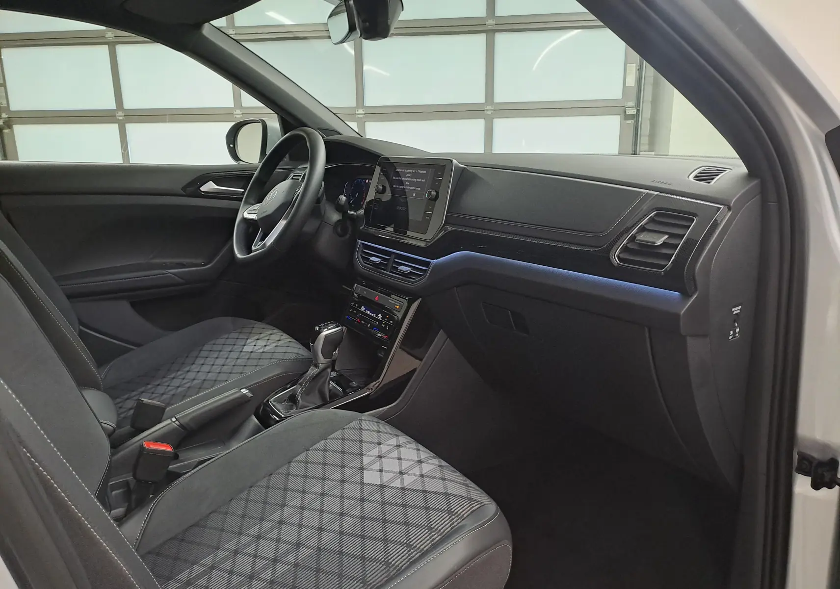 Intérieur côté conducteur du Volkswagen T-Cross 2025 argent, sièges avant chauffants avec motif quadrillé et tableau de bord moderne.