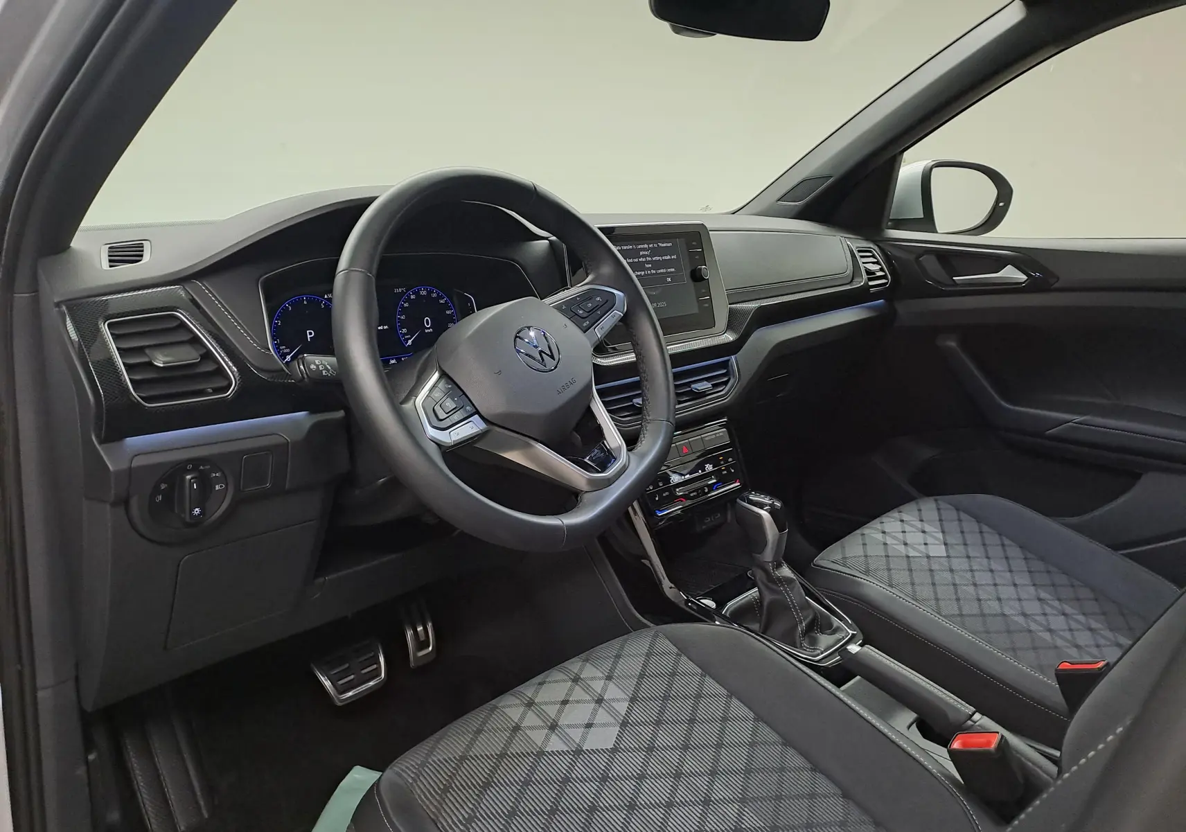 Intérieur du Volkswagen T-Cross 2025, vue côté conducteur, sièges tissu à motif, volant multifonction et console centrale moderne.