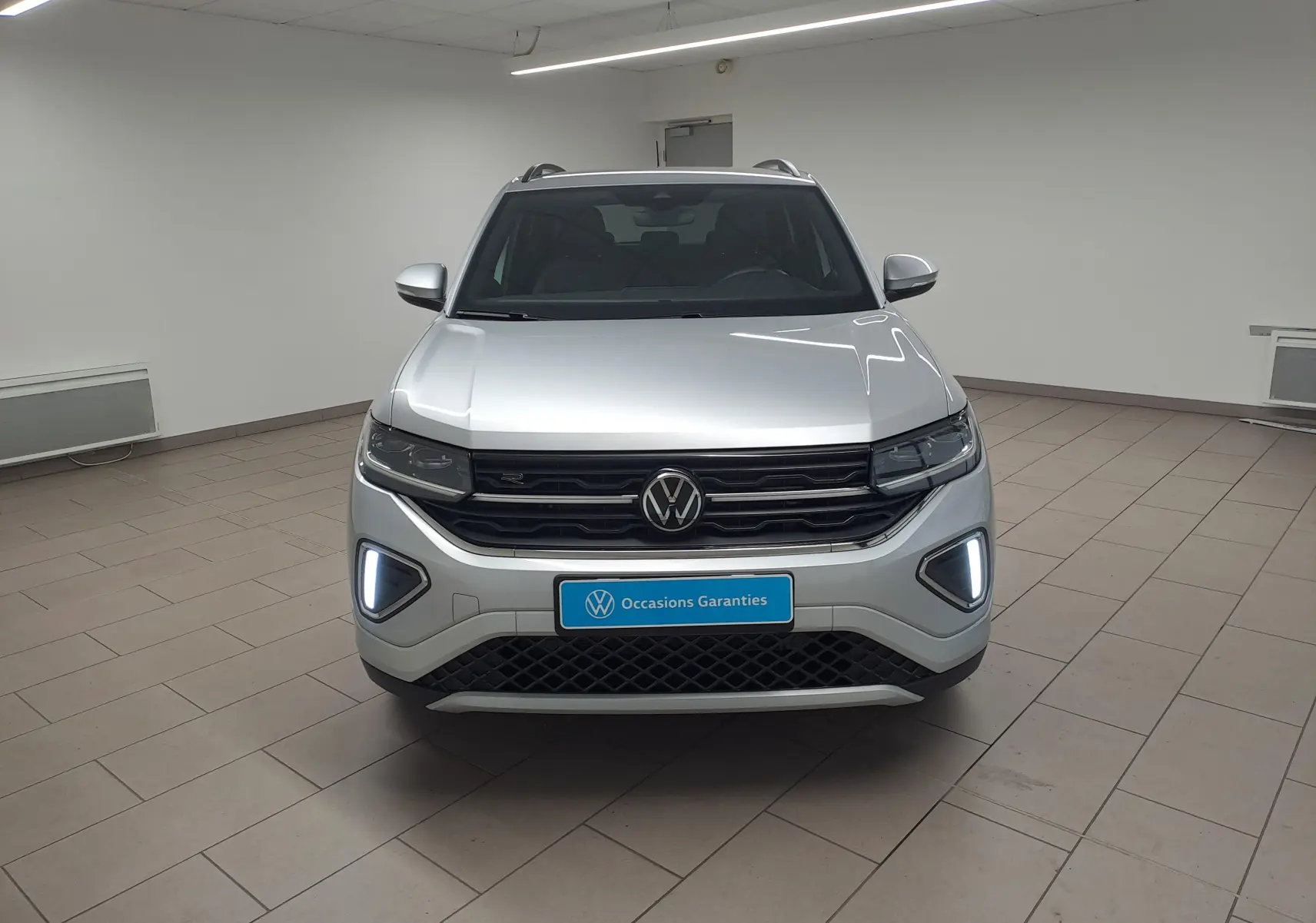 Vue frontale du Volkswagen T-Cross 2025 en Reflet d'Argent avec feux LED et calandre R-Line dans un showroom.