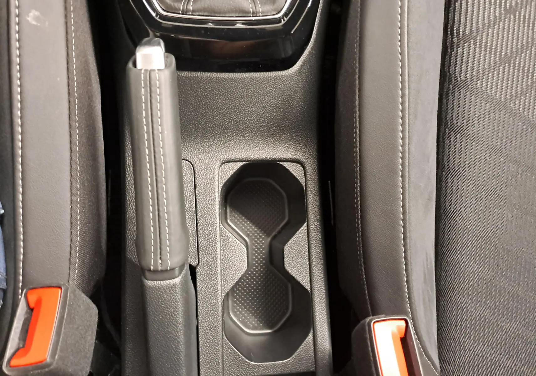 Gros plan sur la console centrale du Volkswagen T-Cross 2025 avec frein à main et porte-gobelets noirs entre les sièges.