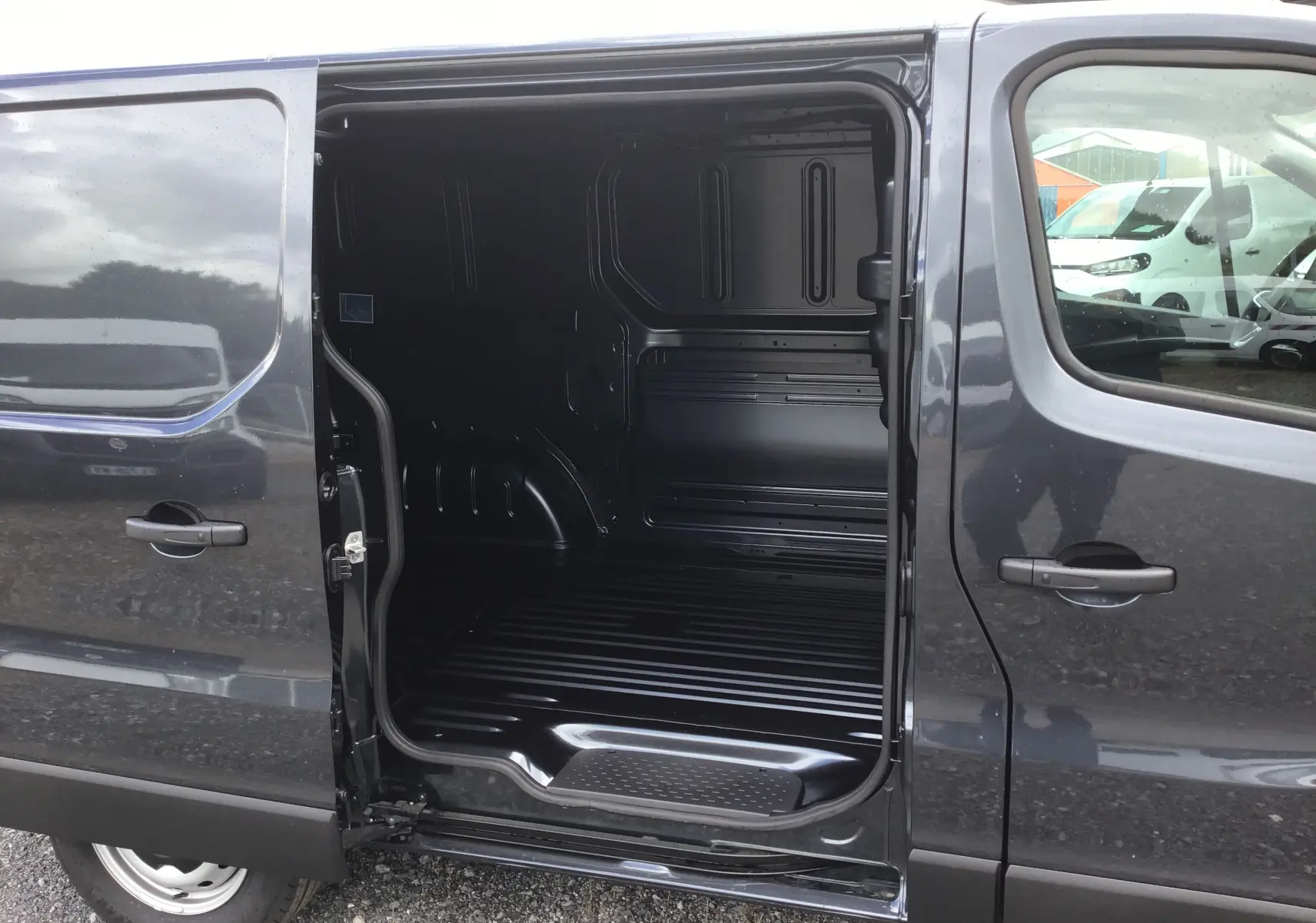 Vue latérale gauche d'un Renault Trafic Fourgon gris comète avec porte coulissante ouverte montrant l'intérieur vide du compartiment de chargement.