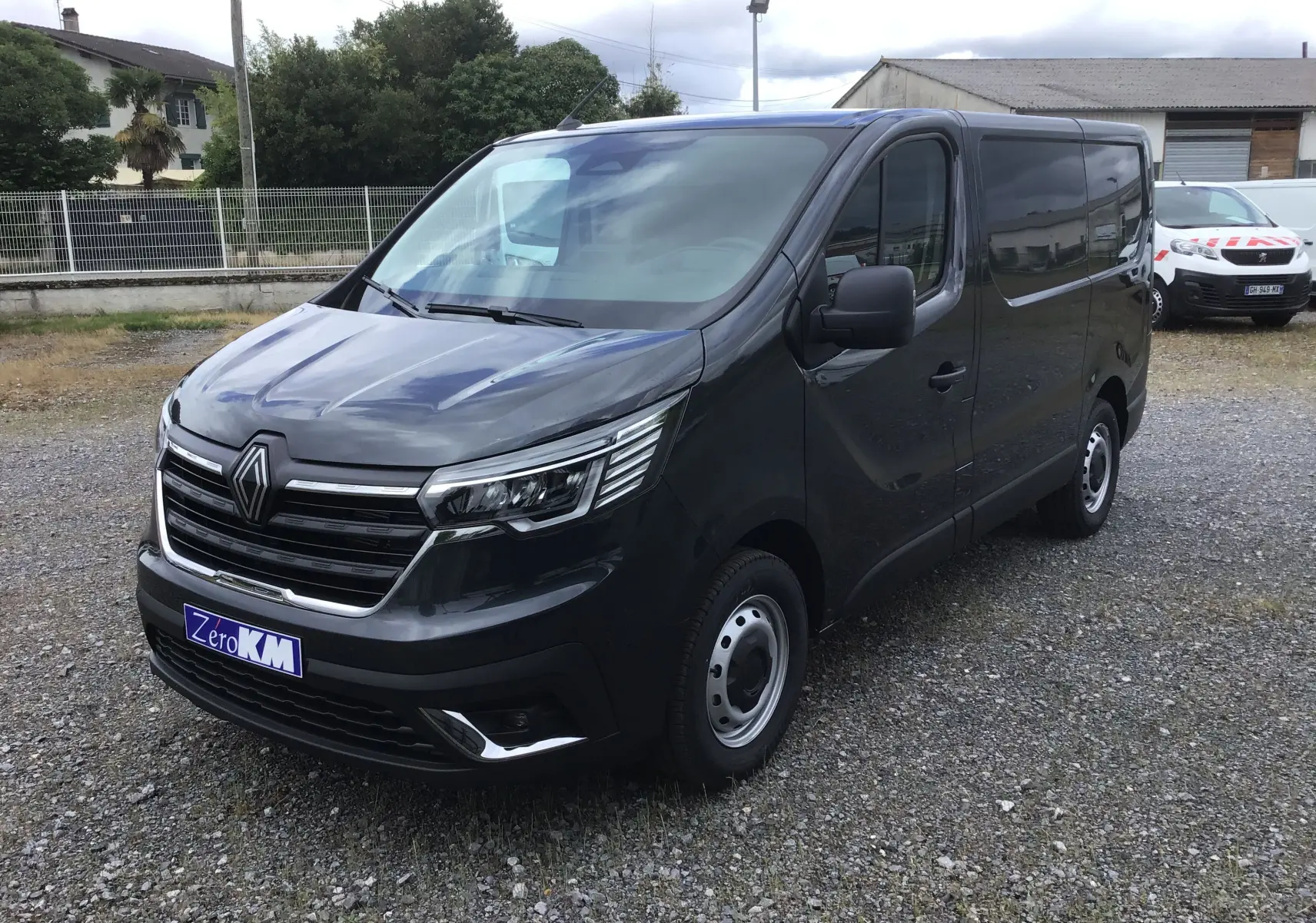 Vue 3/4 avant droit du Renault Trafic Fourgon gris comète avec calandre chromée et phares LED visibles.