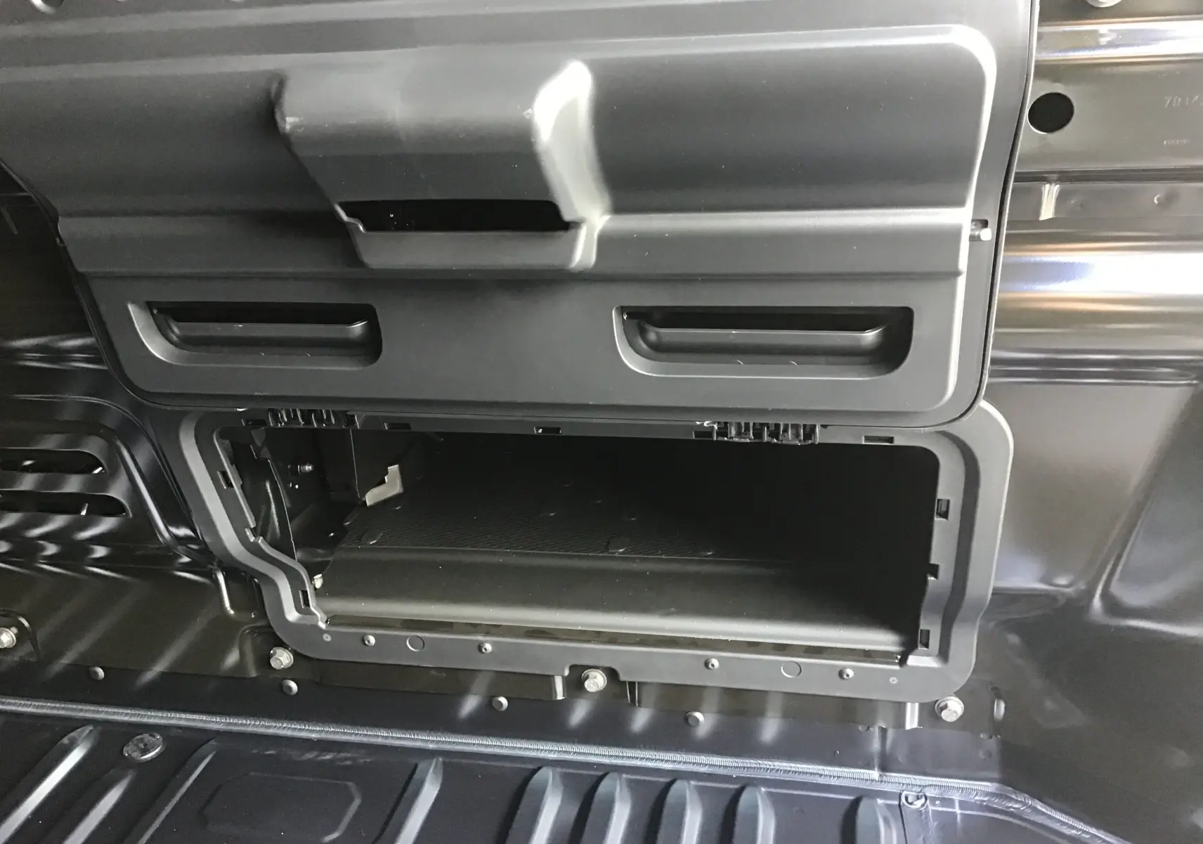 Vue rapprochée du compartiment de rangement intérieur ouvert du Renault Trafic Fourgon gris comète, montrant sa structure en plastique noir.