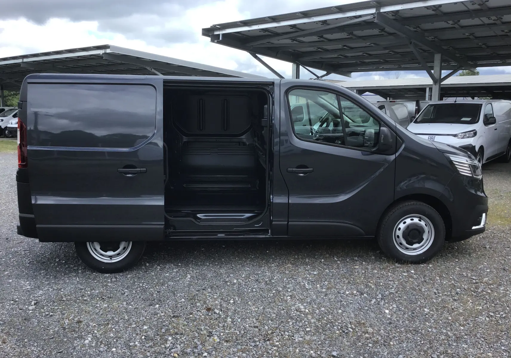 Vue de profil droit d’un Renault Trafic Fourgon gris comète 2025 avec porte latérale coulissante ouverte montrant l’espace de chargement.