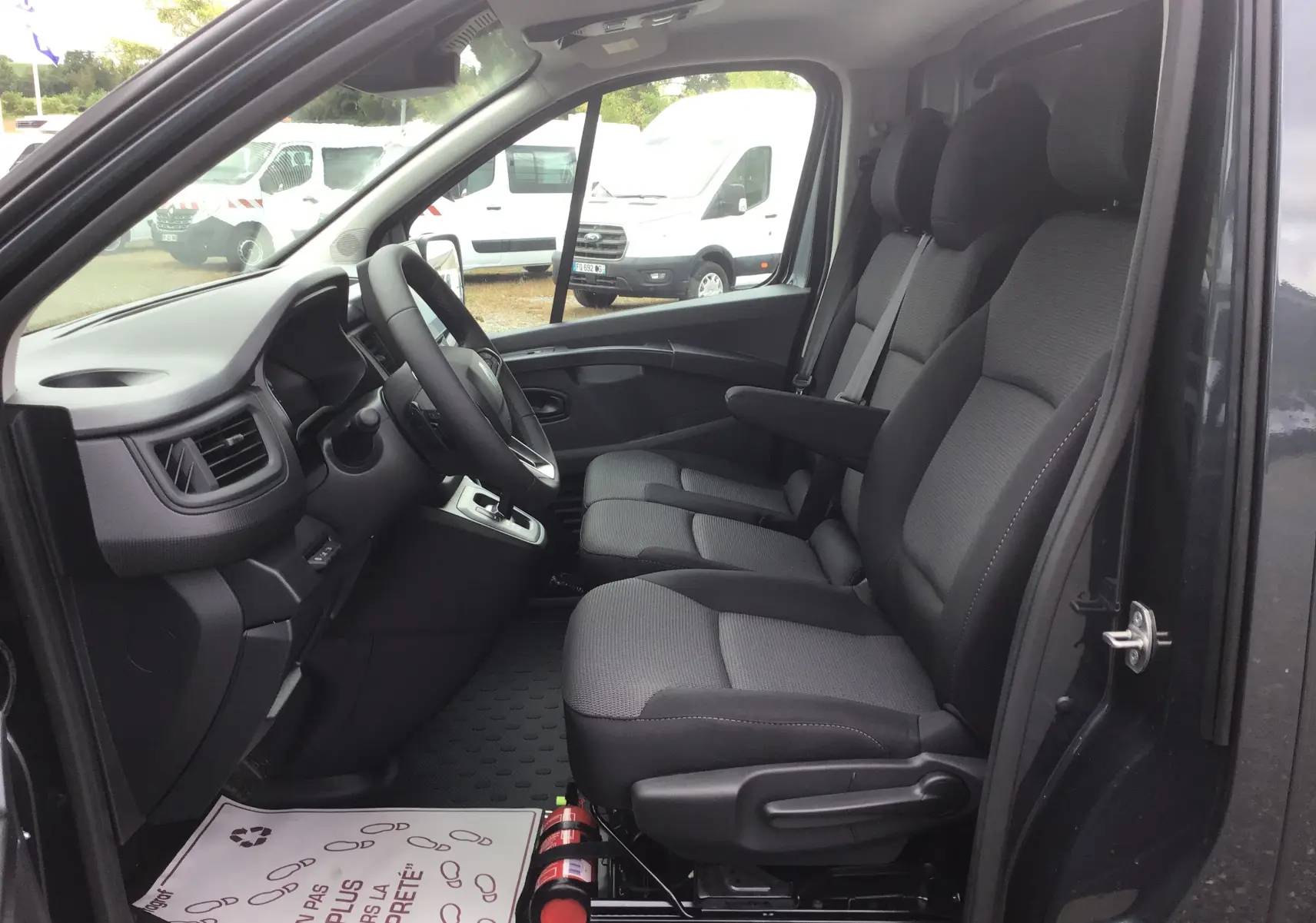 Vue intérieure côté conducteur du Renault Trafic Fourgon gris comète 2025, montrant les sièges avant et le tableau de bord.