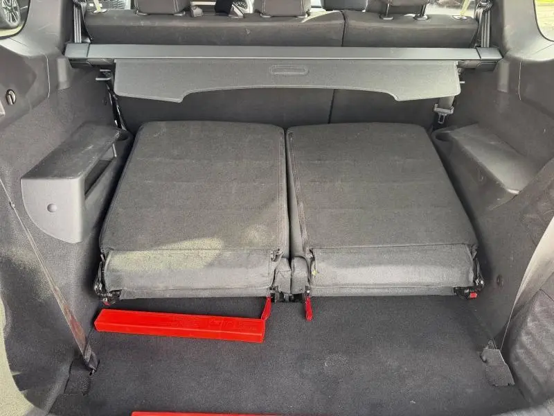 Vue intérieure du coffre du Dacia Jogger 2025 avec sièges arrière rabattus et tapis noir, détail du triangle de sécurité rouge visible.