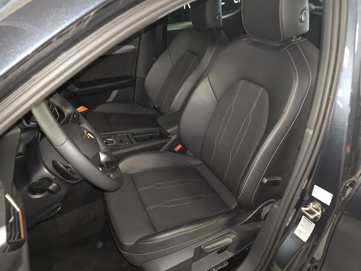 Vue intérieure côté conducteur de la CUPRA Leon gris, sièges sports bimatière noir avec surpiqûres cuivrées.