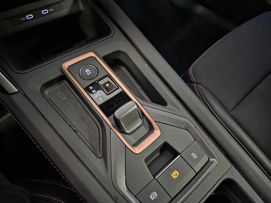 Gros plan sur la console centrale noire avec levier de vitesse et surpiqûres cuivrées dans une CUPRA Leon gris 2025.
