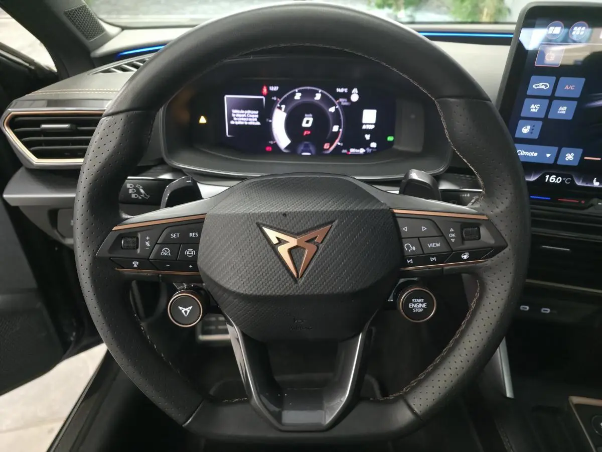 Vue rapprochée du volant cuir perforé noir avec logo CUPRA cuivré et tableau de bord digital du Leon 2.0 TDI gris 2025.