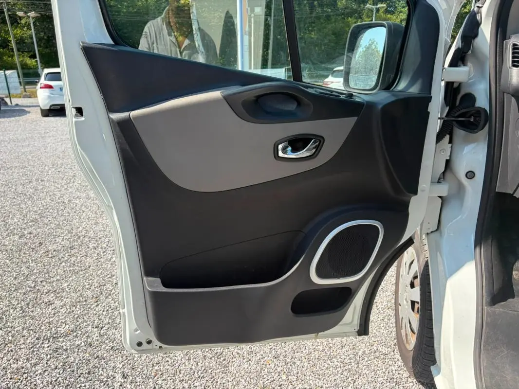 Vue rapprochée de la porte avant droite ouverte du Renault Trafic Fourgon blanc, montrant la garniture intérieure noire et grise avec haut-parleur intégré.