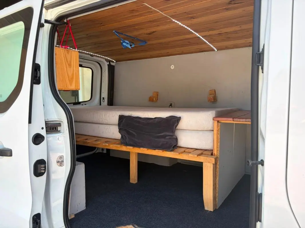 Vue intérieure côté droit du Renault Trafic Fourgon blanc 2018, montrant un aménagement avec lit et plafond en bois.
