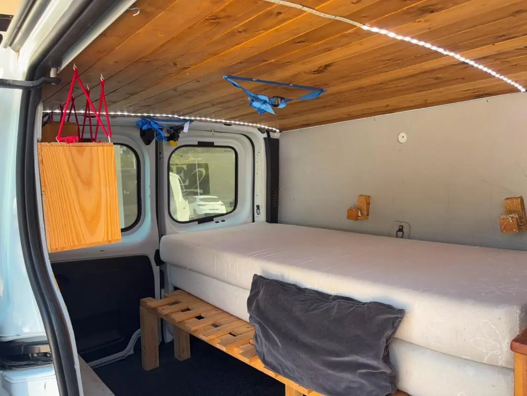 Intérieur du Renault Trafic Fourgon blanc vu de l'arrière, aménagé avec un lit, plafond en bois et éclairage LED.