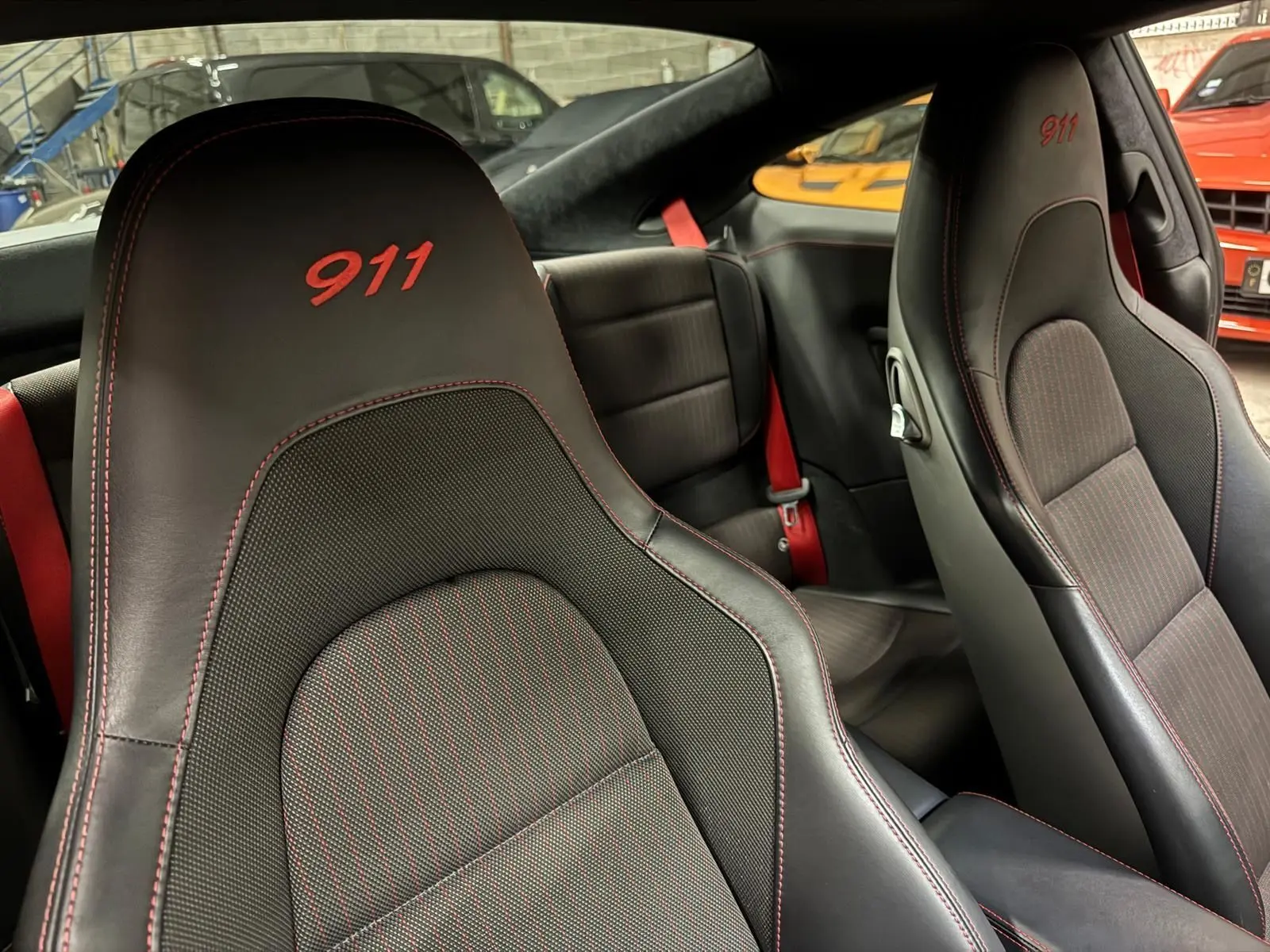 Gros plan sur les sièges avant noirs avec surpiqûres rouges et broderie "911" dans l'habitacle d'une Porsche 911 991.2.