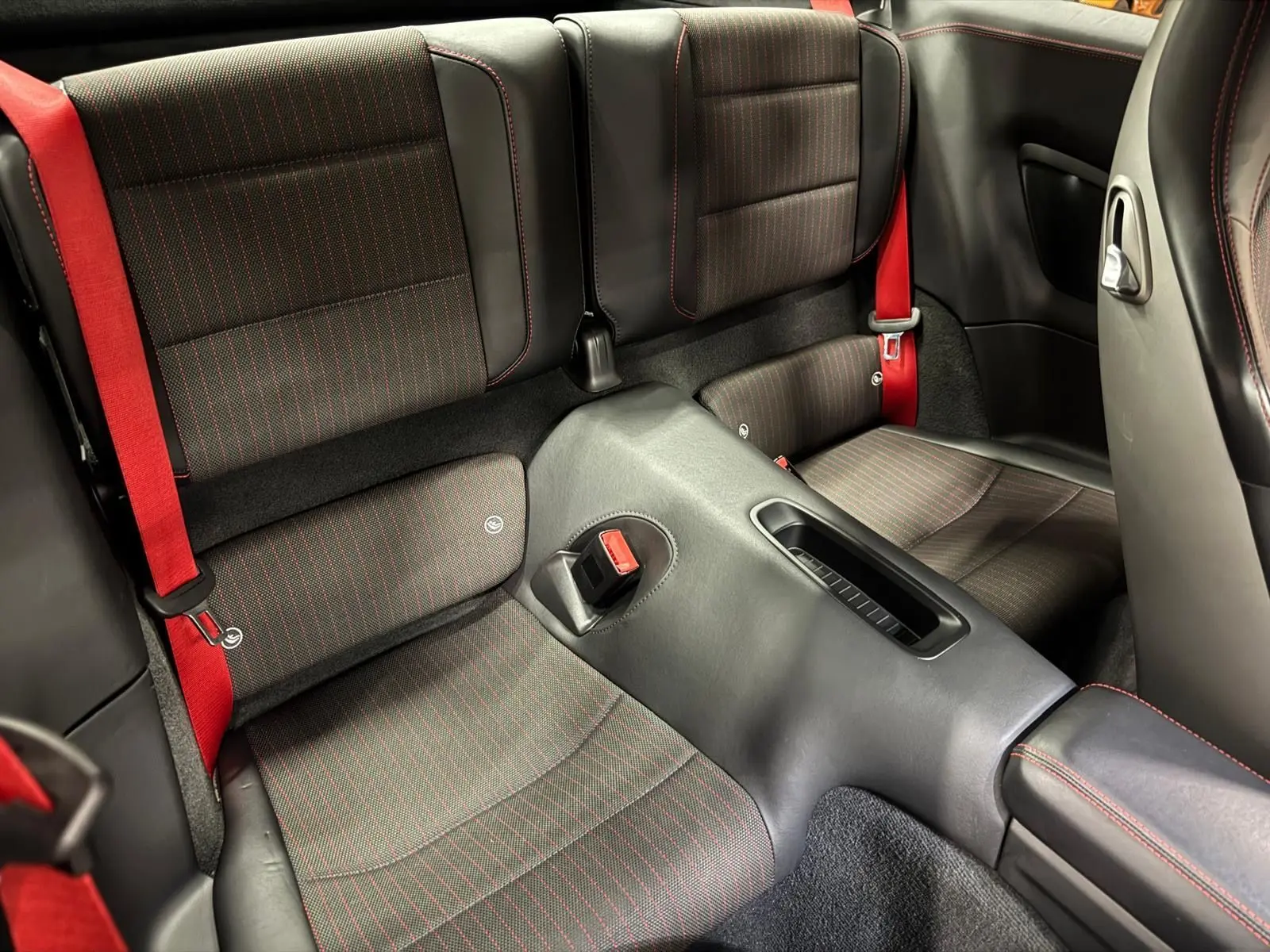 Vue rapprochée de l'arrière intérieur d'une Porsche 911 991 2 Carrera T avec sièges noirs et surpiqûres rouges, ceintures rouges visibles.