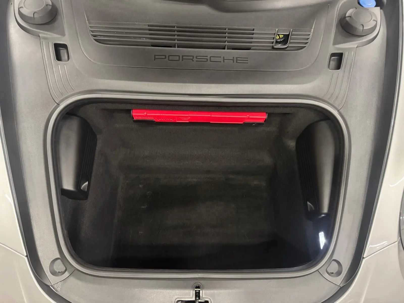 Vue plongeante sur le coffre avant ouvert d'une Porsche 911 991 2 Carrera T gris GT Silver, avec logo Porsche visible.