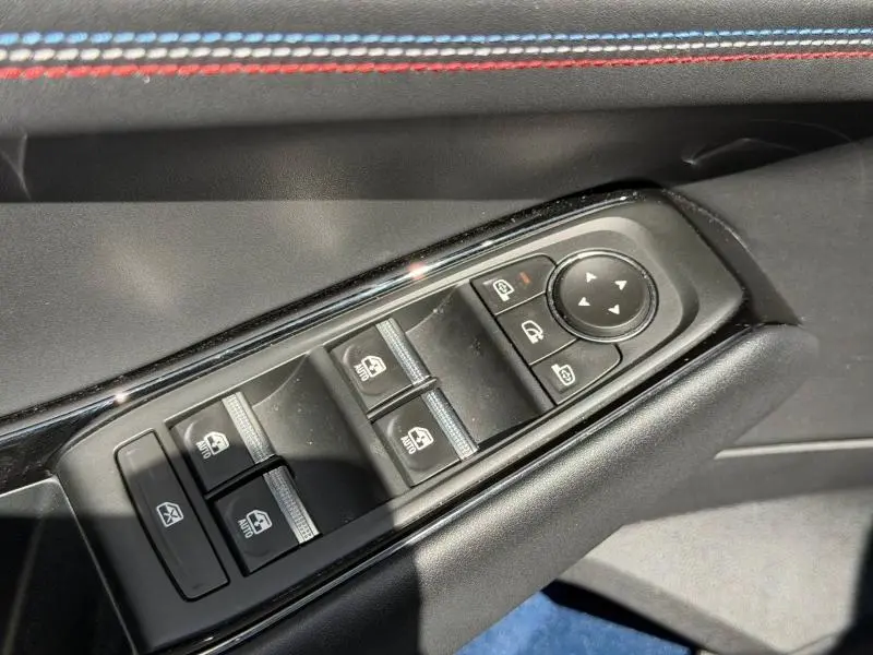 Gros plan sur les commandes des vitres et rétroviseurs côté conducteur du Renault Rafale noir étoilé avec surpiqûres tricolores.