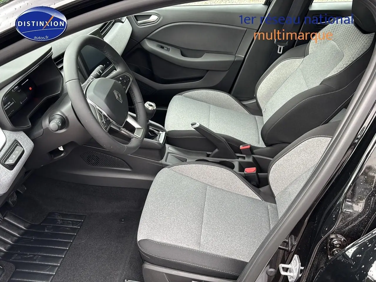 Vue intérieure côté conducteur de la Renault Clio V noire, montrant sièges gris clair et volant multifonction.