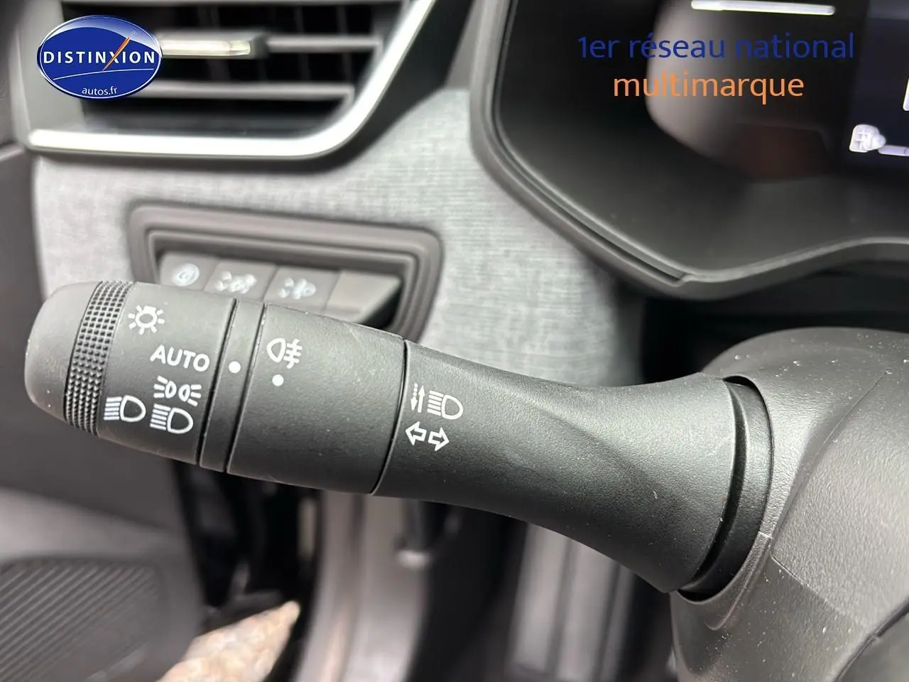 Gros plan sur la commande des phares et clignotants du tableau de bord intérieur d'une Renault Clio V noire.