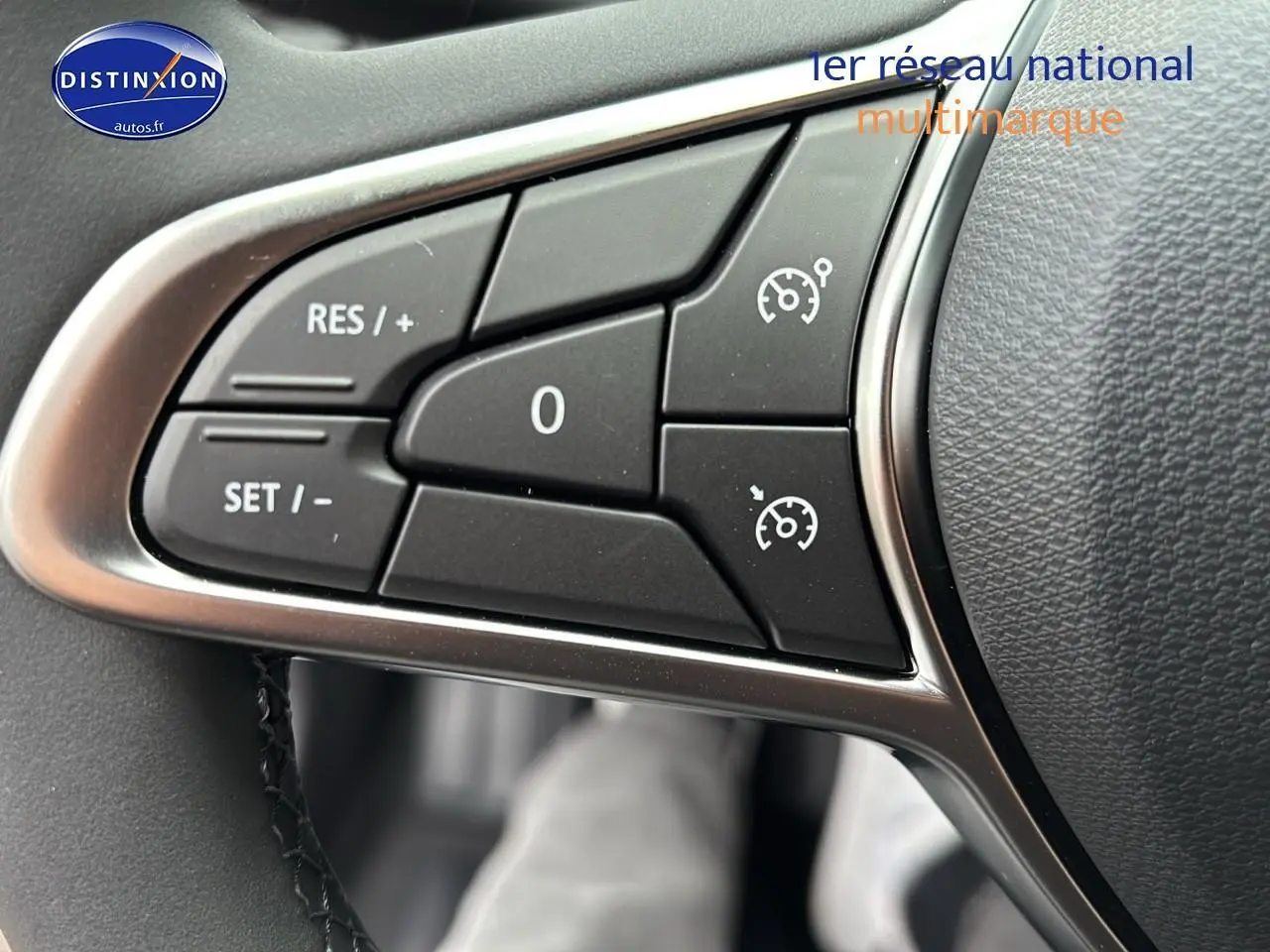 Gros plan sur les commandes du régulateur de vitesse au volant d'une Renault Clio V noire, côté gauche.