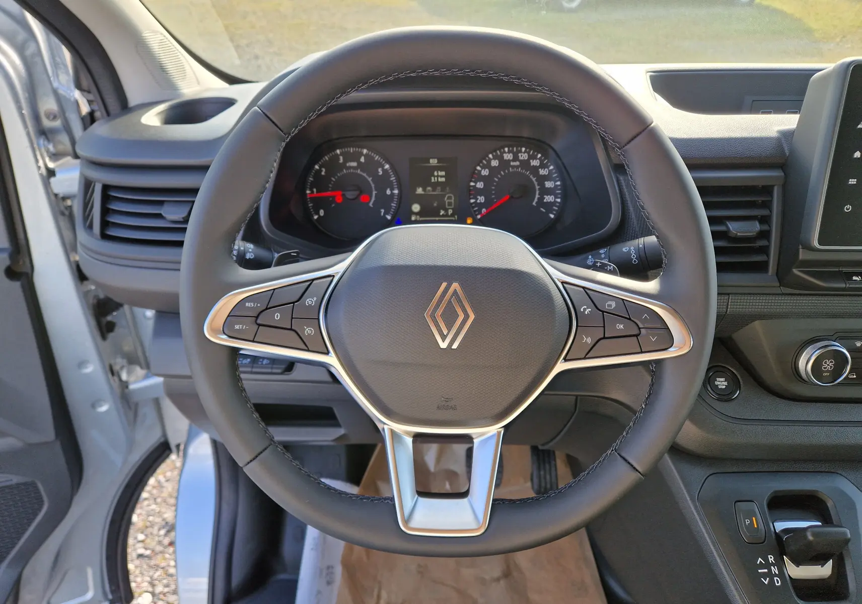 Vue intérieure centrée sur le volant cuir noir du Renault Trafic Fourgon gris Highland avec tableau de bord et commandes visibles.