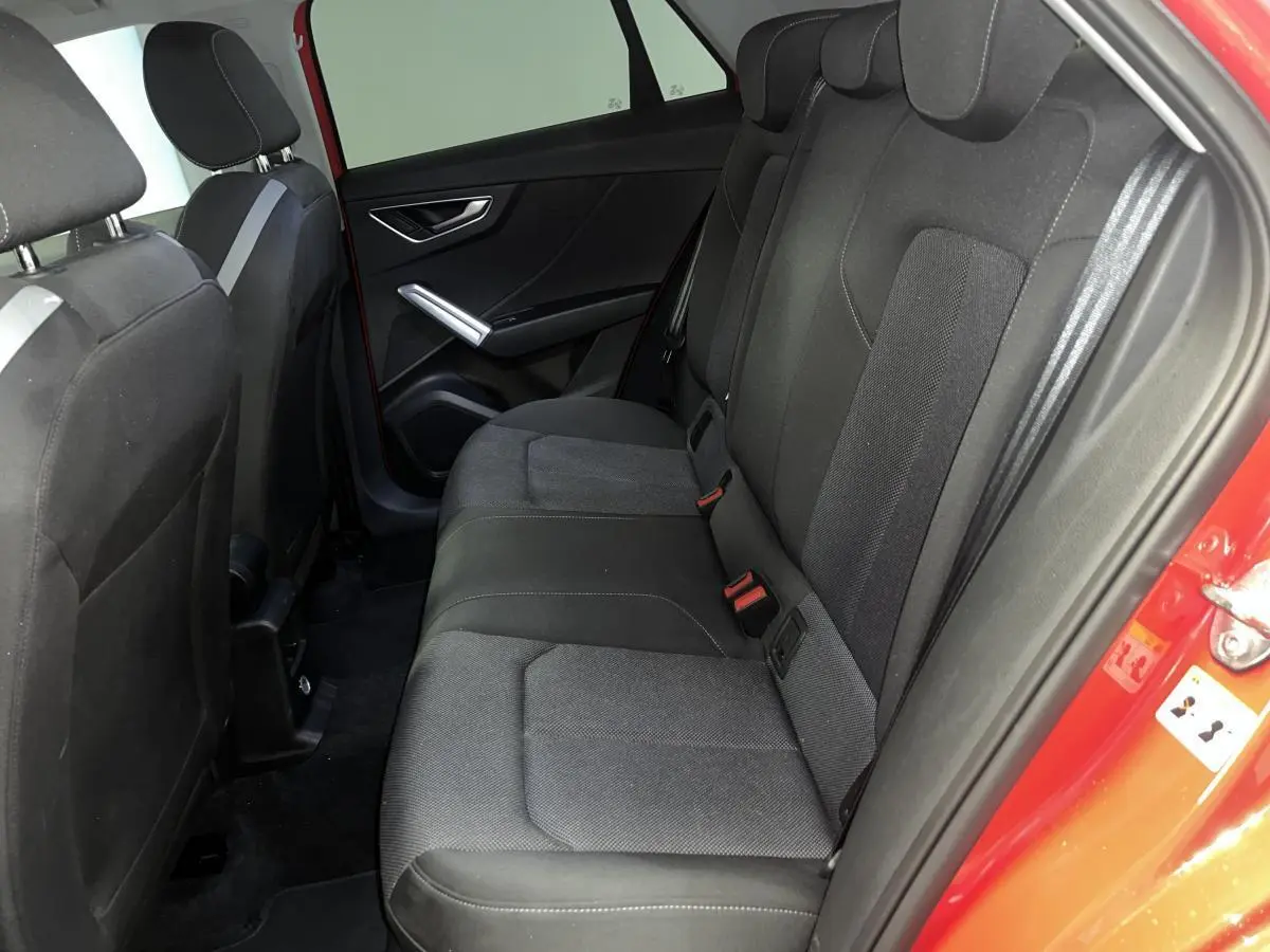 Vue intérieure côté arrière droit d’un Audi Q2 rouge 2024, montrant la banquette arrière en tissu noir avec ceinture de sécurité grise.