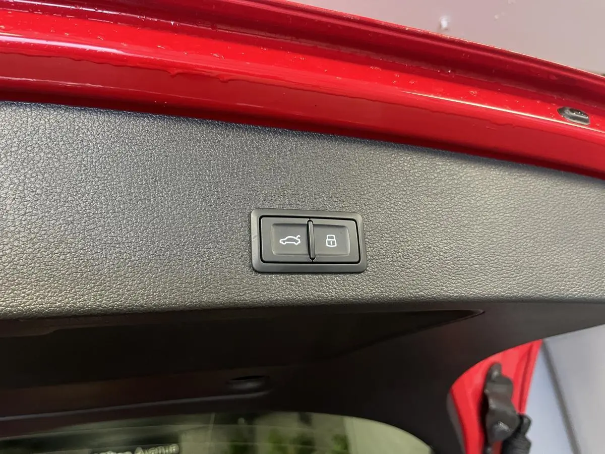 Bouton d'ouverture et de verrouillage du hayon électrique sur la face intérieure du coffre rouge d'un Audi Q2 S line.