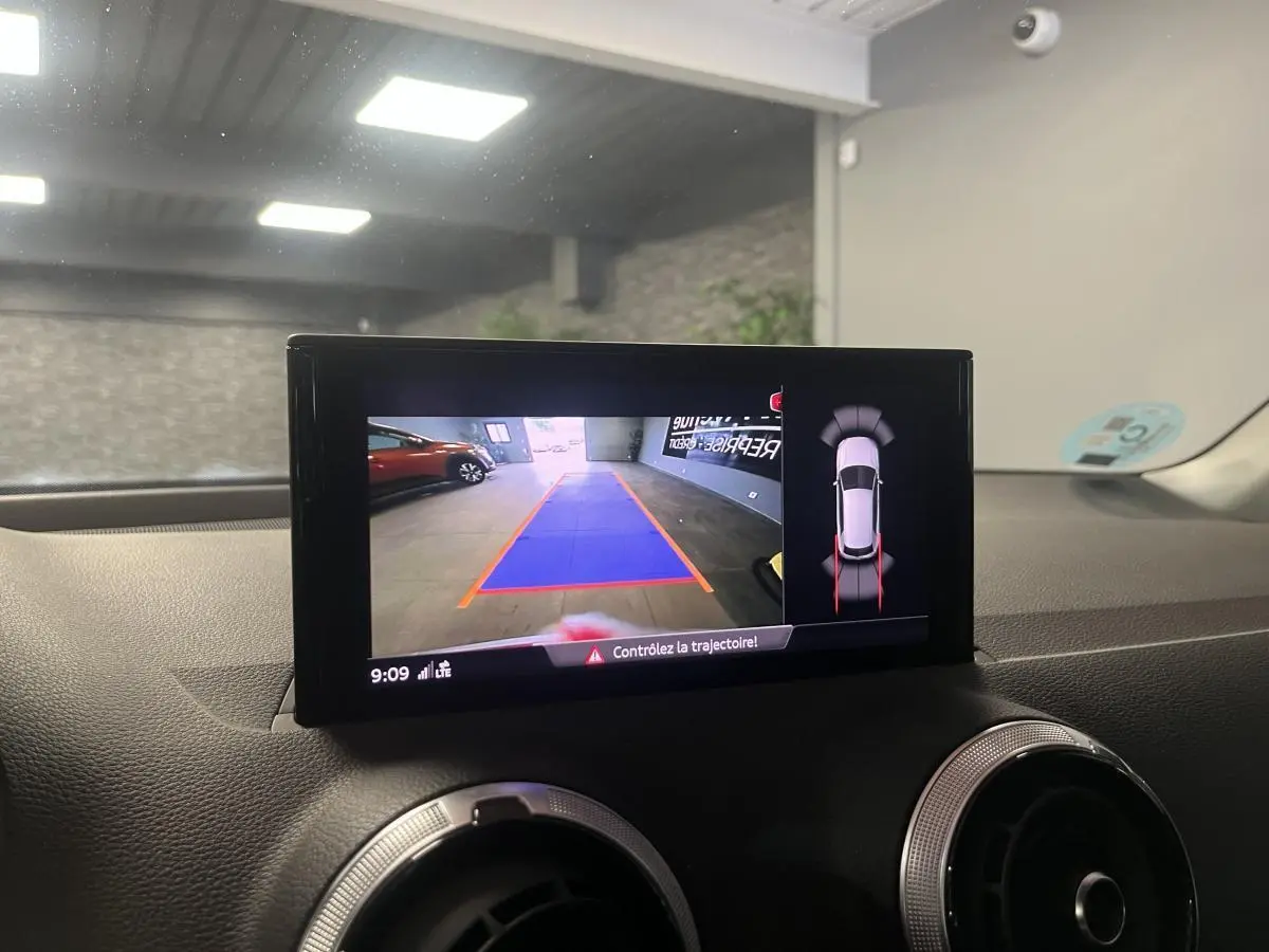 Écran central montrant la caméra de recul et l’aide au stationnement dans un Audi Q2 rouge stationné en intérieur.