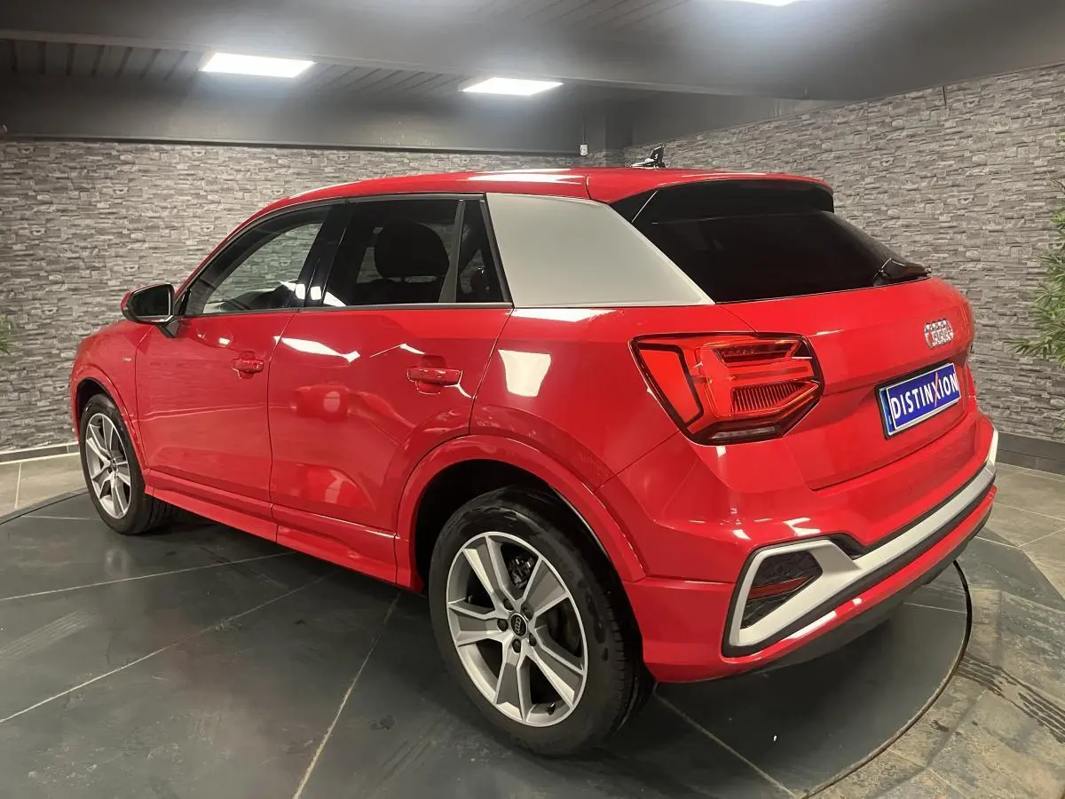 Audi Q2 rouge S line vue 3/4 arrière droit avec toit et montant arrière contrastés gris clair en intérieur showroom.