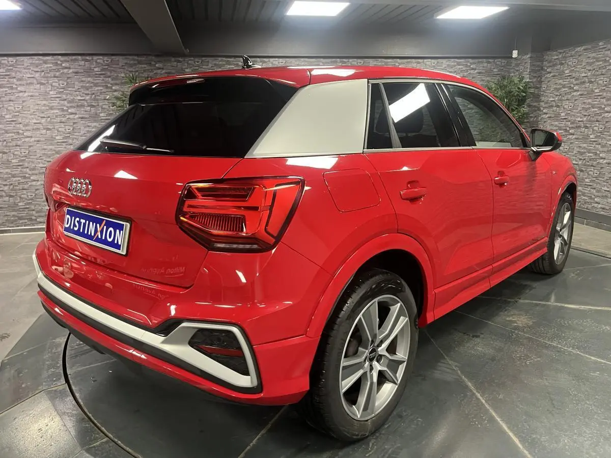 Audi Q2 rouge S line vue 3/4 arrière droit avec toit contrasté blanc et jantes sport 5 branches.