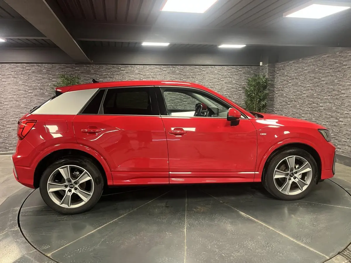 Audi Q2 rouge vue de profil côté gauche, avec toit contrasté blanc et jantes sport 5 branches.