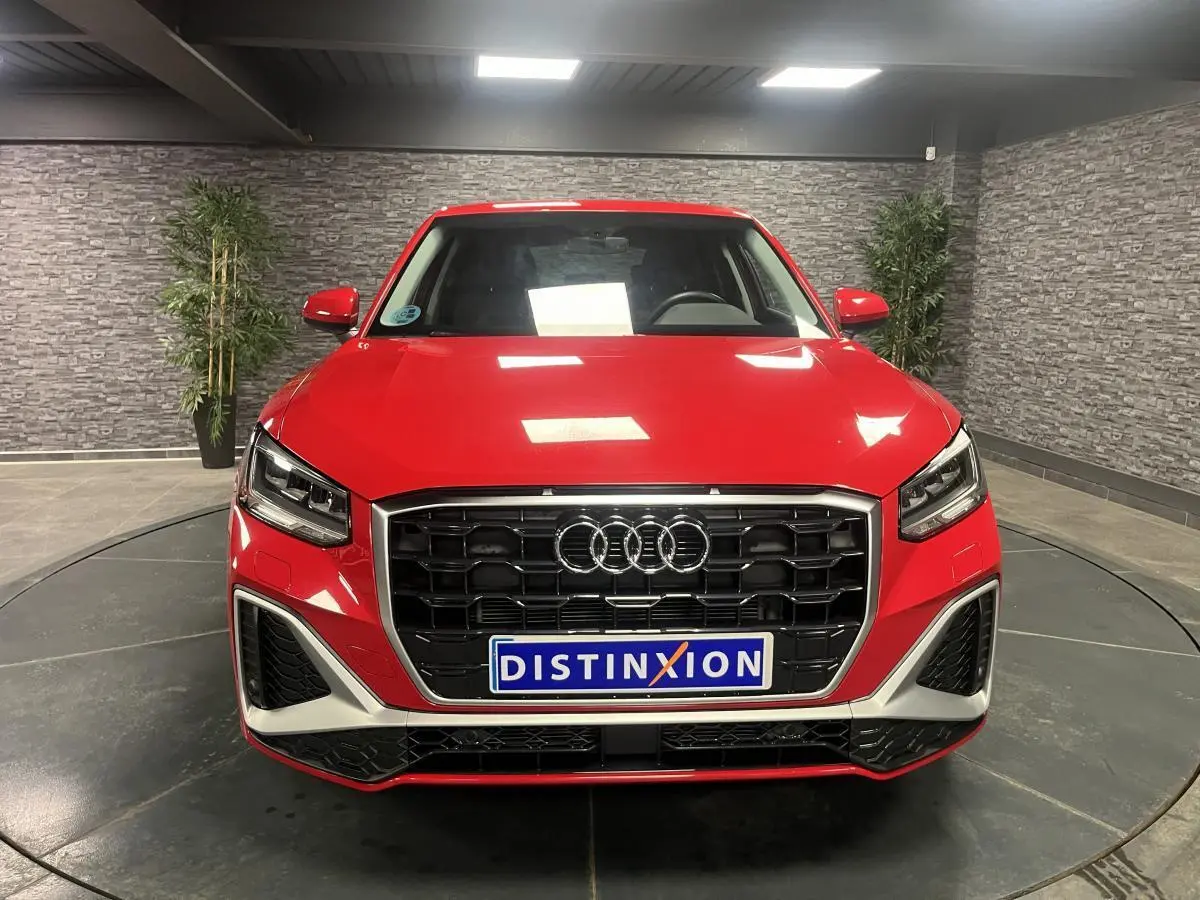 Vue frontale d'un Audi Q2 rouge 2024 avec calandre noire et détails argentés dans un showroom.