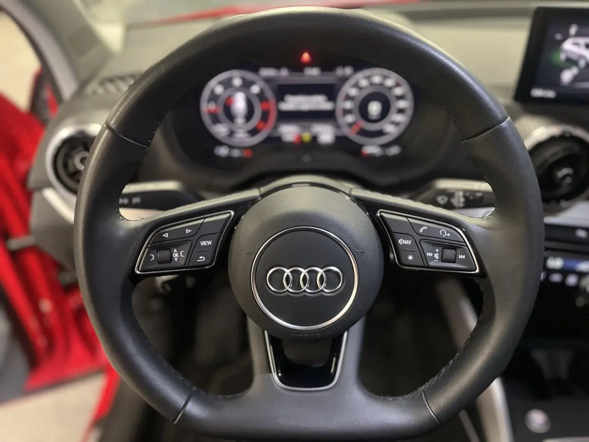 Volant sport en cuir noir avec méplat et commandes multifonctions dans l'Audi Q2 rouge 2024, vue de face intérieure.