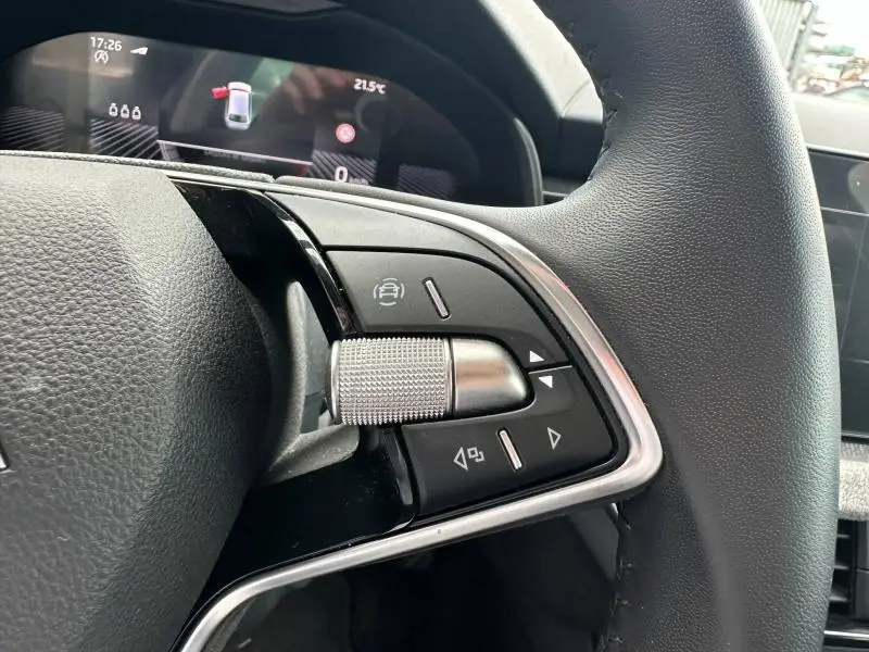 Gros plan sur les commandes multifonctions en aluminium et cuir du volant d'une Skoda Scala gris graphite, tableau de bord en arrière-plan.